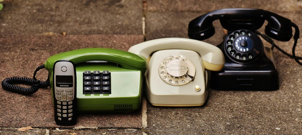 Contact us A variety of antique, vintage, and modern telephones displayed on pavement.